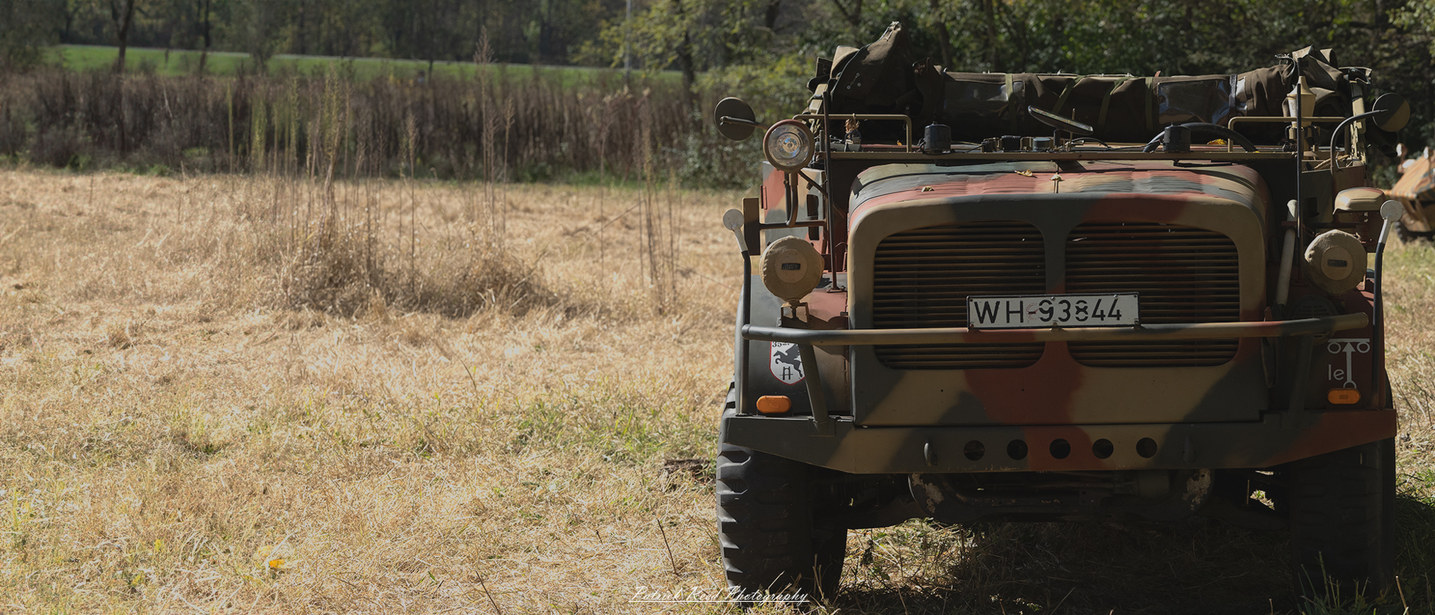 "Image of a German armored car, showcasing its robust and rugged design typical of World War II military vehicles. The armored car is positioned on a dirt road, surrounded by a landscape that suggests a wartime environment, possibly with trees or ruins in the background. The vehicle's camouflage paint is visible, reflecting the military's tactical approach to blending into its surroundings."